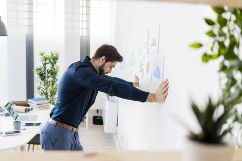 Erschöpfter männlicher Unternehmer, der sich im Büro an die Wand lehnt - GIOF11099