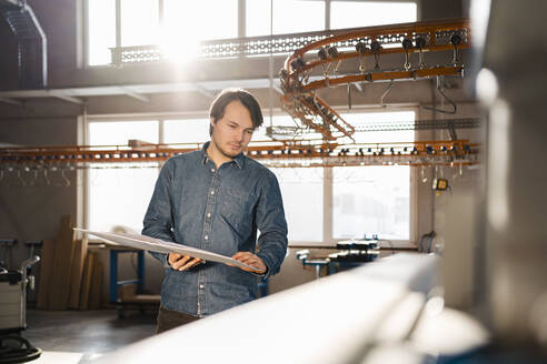 Junger Inspektor, der eine Akte hält, während er am Fließband in der Industrie steht - DIGF14354