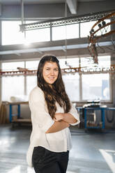 Confident businesswoman smiling while standing with arms crossed at industry - DIGF14356