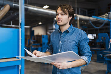 Young inspector with file looking away while standing in industry - DIGF14364