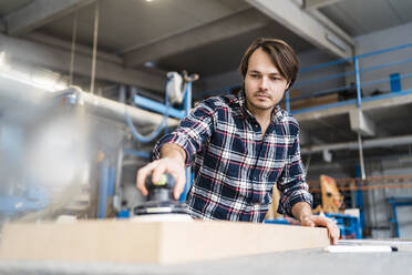 Handwerker bei der Arbeit in der Industrie, der ein Brett mit einer Schleifmaschine bearbeitet - DIGF14374