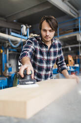 Handwerker beim Schleifen von Holz mit einer Schleifmaschine, während er in der Industrie steht - DIGF14375