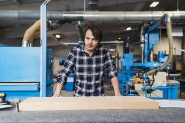 Confident manual worker staring while standing by desk at industry - DIGF14377