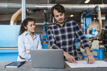 Young businessman with document and laptop working while standing by colleague at industry - DIGF14390