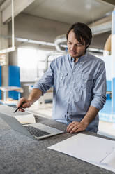 Junger Geschäftsmann mit Laptop bei der Arbeit in der Industrie - DIGF14411