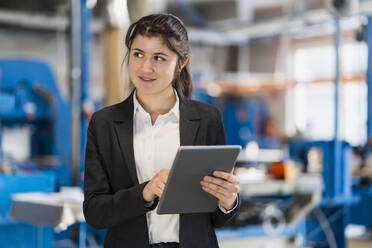Lächelnde Geschäftsfrau mit digitalem Tablet, die wegschaut, während sie in der Industrie steht - DIGF14441