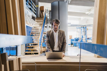 Junger Geschäftsmann arbeitet am Laptop, während er in der Industrie steht - DIGF14449