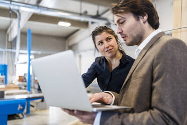 Geschäftsleute diskutieren bei der Arbeit am Laptop in der Industrie - DIGF14454