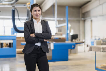 Confident young businesswoman with arms crossed looking away while standing at industry - DIGF14494