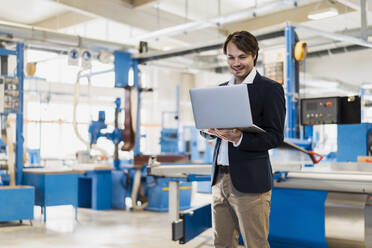 Young entrepreneur using laptop while standing at industry - DIGF14498