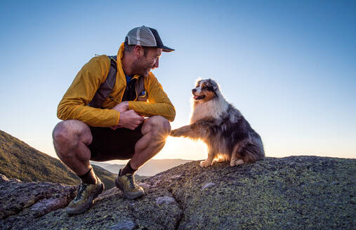Dog paws his owner’s leg during sunrise in the mountains - CAVF92319