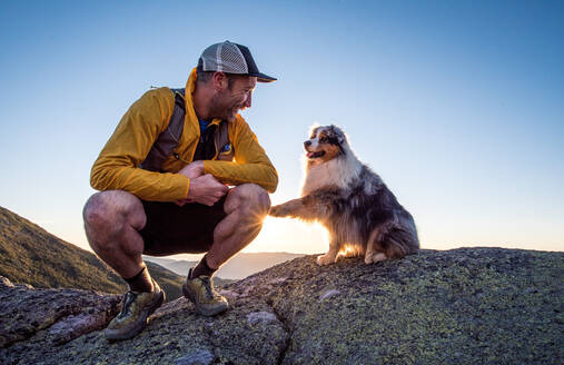 Hund betatscht das Bein seines Besitzers bei Sonnenaufgang in den Bergen - CAVF92319