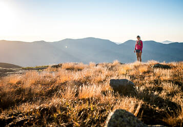 Trailrunnerin bei Sonnenaufgang in den Bergen stehend - CAVF92326