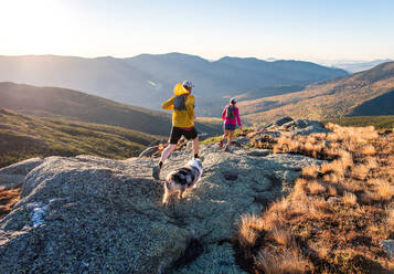 Mann und Frau beim Trailrunning mit Hund in den Bergen bei Sonnenaufgang - CAVF92328