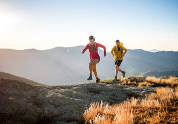 Mann und Frau beim Trailrunning in den Bergen bei Sonnenaufgang - CAVF92330