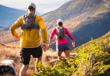 Mann und Frau beim Trailrunning mit Hund in den Bergen bei Sonnenaufgang - CAVF92336