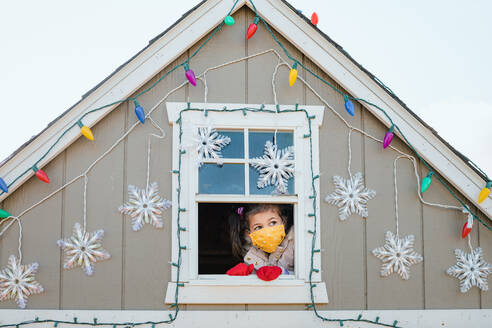 Junges Mädchen mit Gesichtsmaske schaut aus dem Fenster Weihnachtsdekoration - CAVF92400