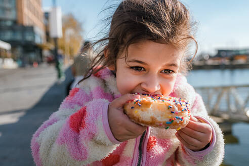 Young girl eating donut with sprinkles outside - CAVF92407