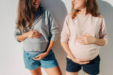 Zwei junge schwangere Frauen halten ihren Bauch und lächeln sich gegenseitig an - CAVF92446