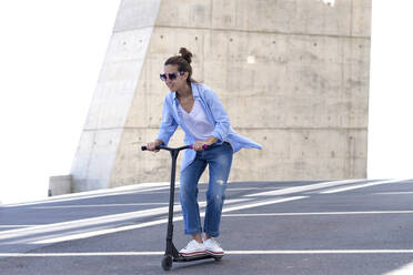 Frau mit Pferdeschwanz und Sonnenbrille auf einem Motorroller in der Stadt - CAVF92451