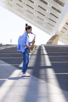 Frau mit Pferdeschwanz, die im Freien stehend ein Saxophon spielt - CAVF92461