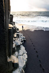 Person walking along Reynisfjara black sand beach at sunset - CAVF92507