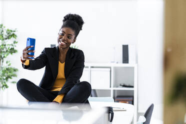 Lächelnde junge Afro-Geschäftsfrau nimmt Selfie durch Smartphone im Büro - GIOF11146