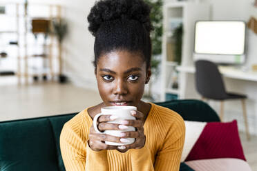 Confident Afro woman with black hair drinking coffee in living room - GIOF11152