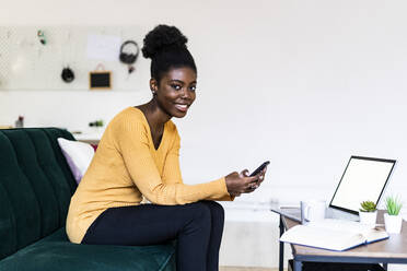 Lächelnde Afro-Frau mit Smartphone zu Hause - GIOF11159