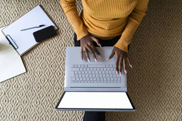 Junge Frau benutzt einen Laptop, während sie zu Hause auf einem Teppich sitzt - GIOF11169