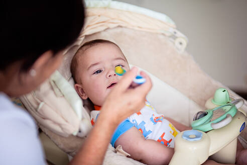 Das Baby erhält seine erste feste Mahlzeit mit einem blauen Löffel. - CAVF92523