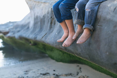 Brüder sitzen auf einem großen Felsen am Strand - Fokus auf ihre nackten Füße - CAVF92525