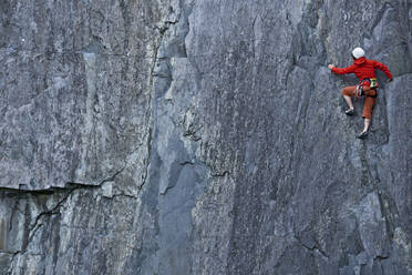 Frau klettert in einem Schiefersteinbruch in Nordwales eine steile Felswand hinauf - CAVF92571