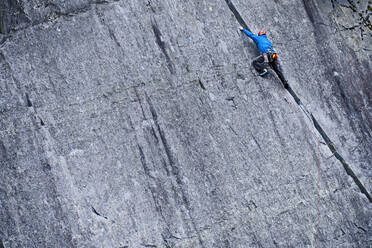 Mann klettert in einem Schiefersteinbruch in Nordwales eine steile Felswand hinauf - CAVF92573