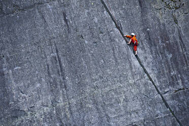 Frau klettert in einem Schiefersteinbruch in Nordwales eine steile Felswand hinauf - CAVF92575