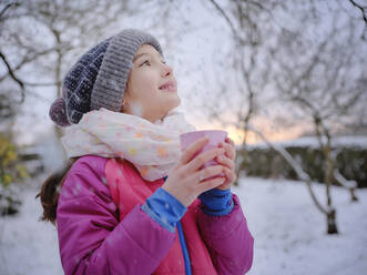 Lächelndes Mädchen in warmer Kleidung hält Teetasse im Winter - DIKF00557