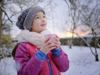 Nachdenkliches Mädchen mit Teetasse und warmer Kleidung bei Sonnenuntergang im Winter - DIKF00558