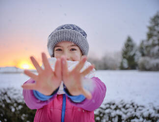 Fröhliches Mädchen in warmer Kleidung zeigt Hände bei Sonnenuntergang im Winter - DIKF00560