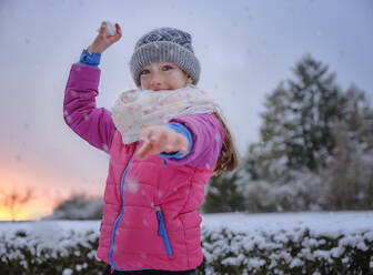 Playful girl throwing snowball in snow during winter - DIKF00561