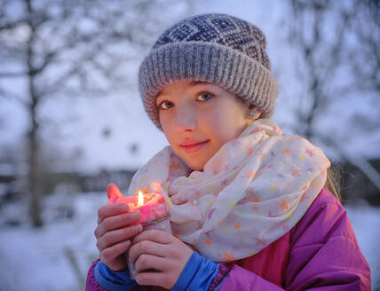 Nettes Mädchen in warmer Kleidung, das eine brennende Kerze im Winter hält - DIKF00562