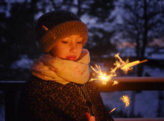 Mädchen in warmer Kleidung mit Wunderkerze in der Abenddämmerung im Winter - DIKF00563