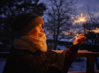 Playful girl in warm clothing holding sparkler during winter - DIKF00564