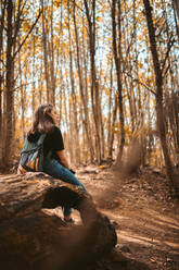 Alternative Frau, die sich auf einem Baum ausruht und den schönen Wald betrachtet - CAVF92588