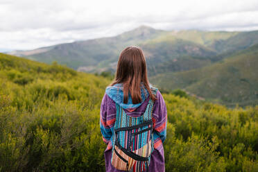 Junge Frau mit alternativer Kleidung Blick auf einen großen grünen Berg - CAVF92589