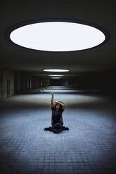 Woman sitting in a building under the light of a skylight. - CAVF92614