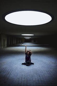 Frau, die in einem Gebäude unter dem Licht eines Oberlichts sitzt. - CAVF92614