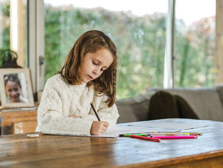Crop little girl drawing with multicolored pencils on paper sheet in light room - ADSF20675