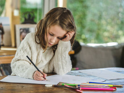 Crop little girl drawing with multicolored pencils on paper sheet in light room - ADSF20676