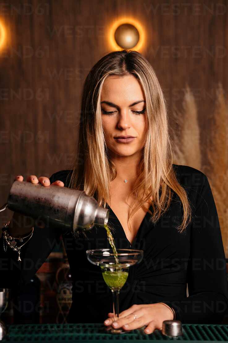 Wineglass stands on bar and woman bartender holds mixing cup and