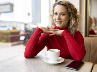 Dreamy female sitting at table in cafe and drinking hot beverage while enjoying weekend and looking at camera - ADSF20714